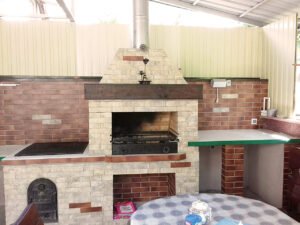 Grill ogrodowy wyłożony jest kamieniem naturalnym, płytkami ceramicznymi i elementami drewnianymi.