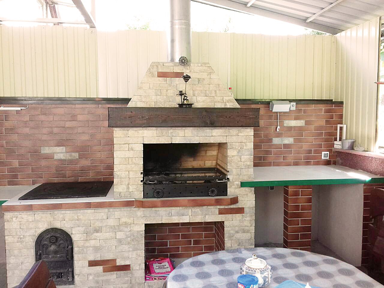 Grill ogrodowy wyłożony jest kamieniem naturalnym, płytkami ceramicznymi i elementami drewnianymi.