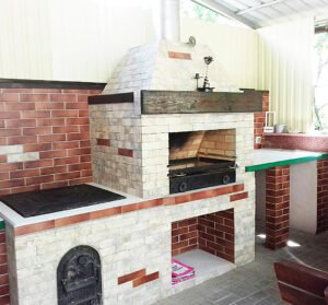 Grill ogrodowy wyłożony jest kamieniem naturalnym, płytkami ceramicznymi i elementami drewnianymi.