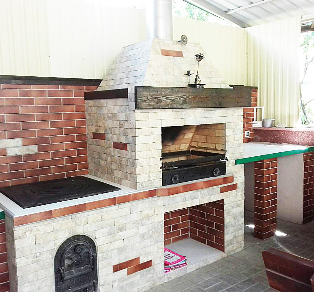 Grill ogrodowy wyłożony jest kamieniem naturalnym, płytkami ceramicznymi i elementami drewnianymi.