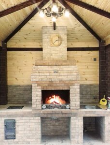 Grill ogrodowy wyłożony jest kamieniem naturalnym, płytkami ceramicznymi i elementami drewnianymi.