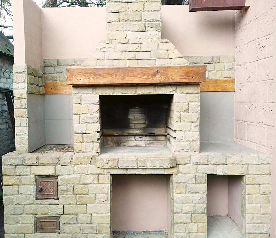 Grill ogrodowy wyłożony jest kamieniem naturalnym, płytkami ceramicznymi i elementami drewnianymi.