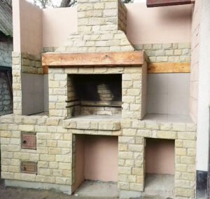 Grill ogrodowy wyłożony jest kamieniem naturalnym, płytkami ceramicznymi i elementami drewnianymi.