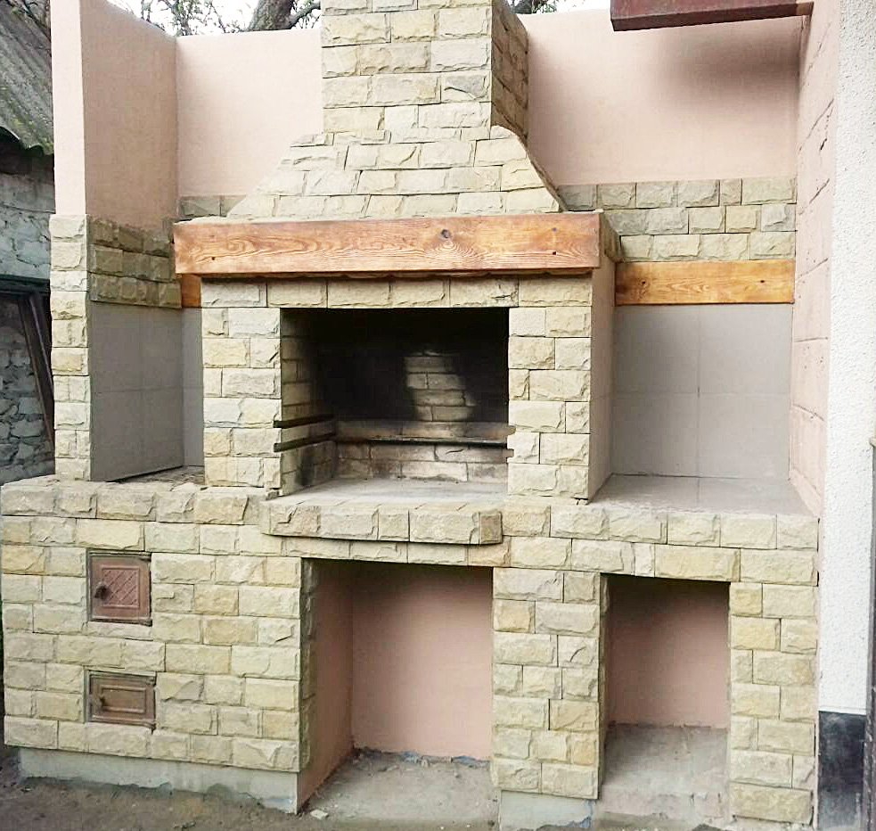 Grill ogrodowy wyłożony jest kamieniem naturalnym, płytkami ceramicznymi i elementami drewnianymi.