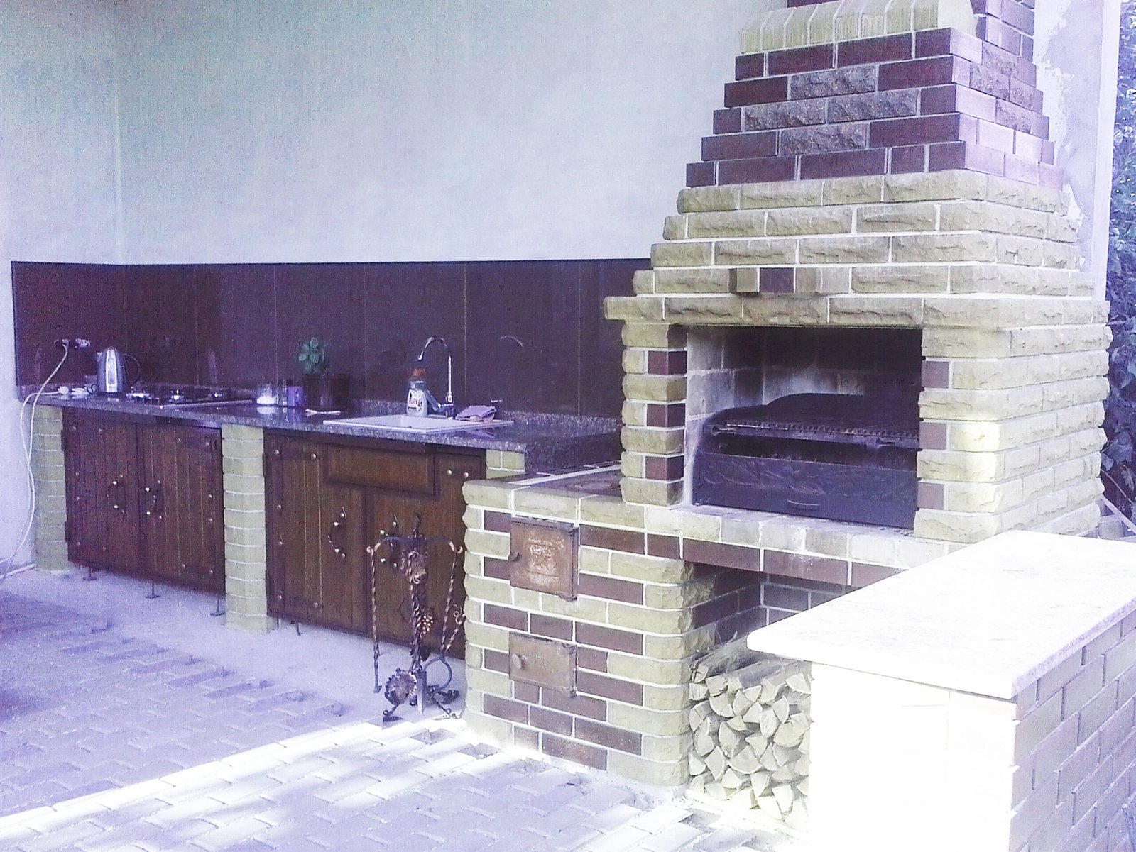 Grill ogrodowy wyłożony jest kamieniem naturalnym, płytkami ceramicznymi i elementami drewnianymi.