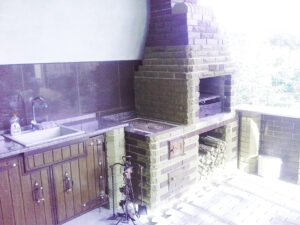 Grill ogrodowy wyłożony jest kamieniem naturalnym, płytkami ceramicznymi i elementami drewnianymi.