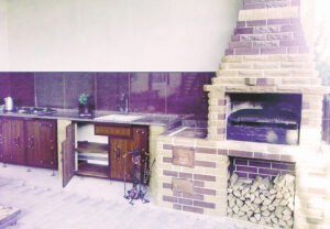 Grill ogrodowy wyłożony jest kamieniem naturalnym, płytkami ceramicznymi i elementami drewnianymi.