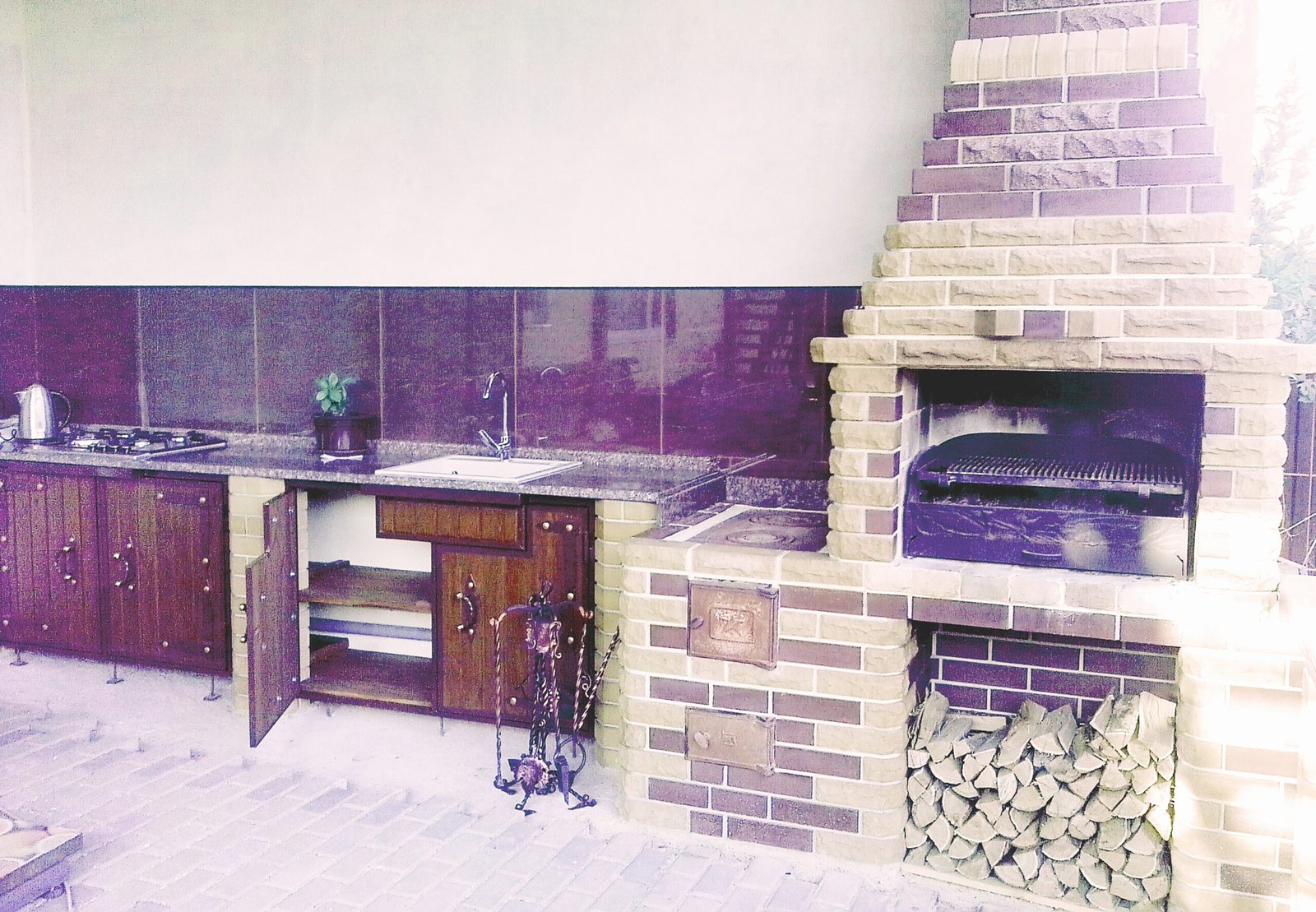 Grill ogrodowy wyłożony jest kamieniem naturalnym, płytkami ceramicznymi i elementami drewnianymi.