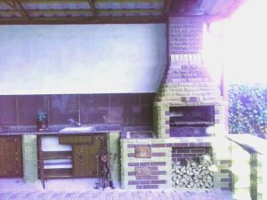 Grill ogrodowy wyłożony jest kamieniem naturalnym, płytkami ceramicznymi i elementami drewnianymi.