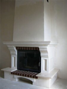 Kominek wykończony jest gipsowymi elementami dekoracyjnymi i pomalowany.