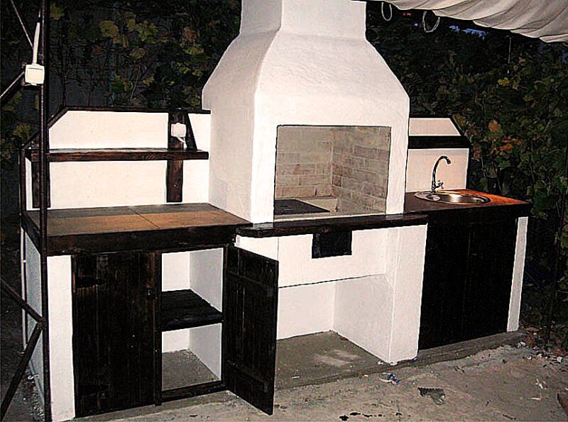 Grill ogrodowy jest otynkowany i pomalowany. Zawiera dekoracyjne elementy drewniane.